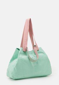 Große Tragetasche aus mintgrünem Stoff mit zwei rosa Baumwollgriffen. Das Design verfügt über eine weiche, strukturierte Form und sichtbare Nähdetails.