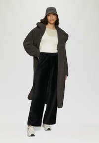 Overmaatse donkergrijze fleecejas, crèmekleurige tanktop, zwarte velours wijde broek, grijze pet en lichte sneakers met accenten. Zachte texturen en casual stijl.