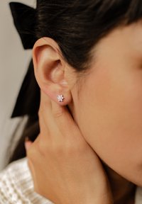 Orecchini a forma di fiore in argento con piccole gemme, indossati all'orecchio di un modello, che mostrano un primo piano del design e dei dettagli.
