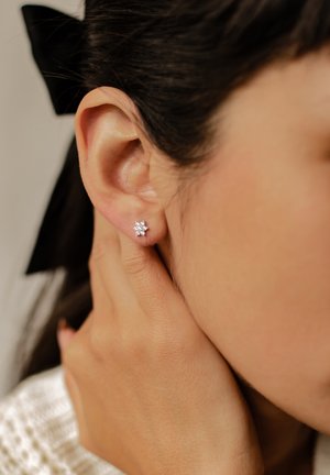 Orecchini a forma di fiore in argento con piccole gemme, indossati all'orecchio di un modello, che mostrano un primo piano del design e dei dettagli.