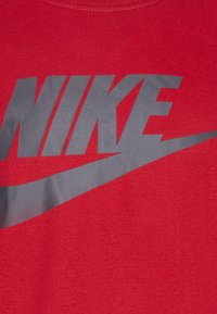 Camiseta roja con un gran logo gris de Nike, que presenta una textura suave y un diseño de cuello redondo. El logo incluye un elemento de swoosh.