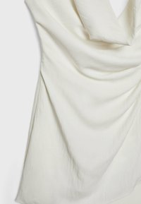 Tissu blanc drapé avec une texture douce, présentant des lignes lisses et fluides ainsi qu'un éclat subtil. Le matériau a une apparence légère et aérienne.