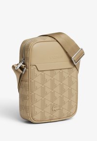 Bolso bandolera beige con textura y patrón geométrico, cierre de cremallera y correa ajustable; con logotipo en relieve en el frente.