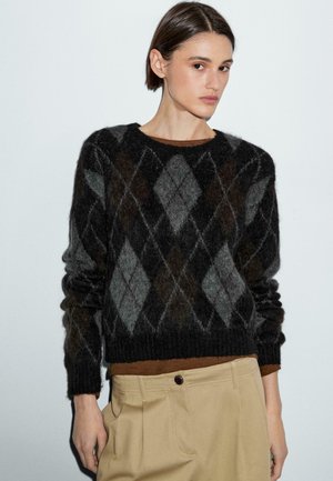 Pullover a motivo argyle in nero e grigio, realizzato in materiale morbido, con collo a giro che presenta polsini a coste, indossato sopra una maglietta marrone.