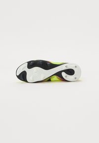 Crampon de football avec un dessus noir et jaune vif, surface texturée et motif de pointes distinct sur la semelle blanche pour l'adhérence.