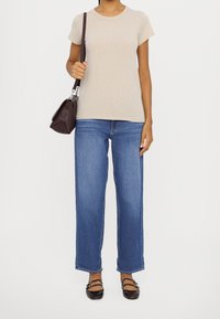 Beige t-shirt met korte mouwen gecombineerd met lichtblauwe wijde jeans. Accessoires zijn een kleine bruine crossbody tas en donkere platte schoenen.