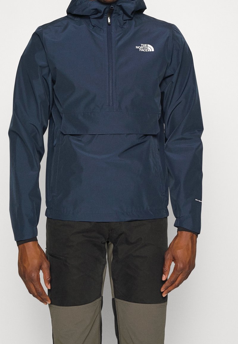 Giacca a pullover blu navy con cappuccio, materiale resistente all'acqua, zip frontale e tasca frontale. Presenta il logo sul petto e un design aerodinamico.