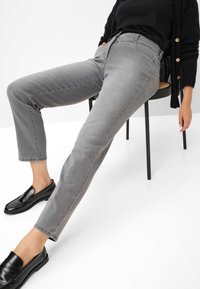 Jeans in denim grigio con un taglio affusolato, caratterizzati da una vita media, design a cinque tasche e una lieve texture. Abbinati a mocassini neri.