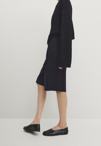 Maglione nero di grandi dimensioni con texture, gonna nera al ginocchio e scarpe nere basse. Design semplice e minimalista con una vestibilità rilassata.