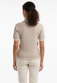 Beżowy krótki sweter z dzianiny z warkoczowym wzorem, z białymi prążkowanymi wykończeniami na mankietach i krawędzi, nadającymi mu uporządkowany wygląd.