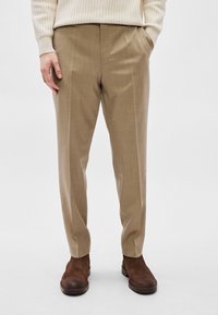 Μπεζ παντελόνι με ραφή, με απαλή υφή, που διαθέτει πιέτες στο μπροστινό μέρος και στενή γραμμή. Συνδυάζεται με καφέ καστόρινες μποτάκια μέχρι τον αστράγαλο.