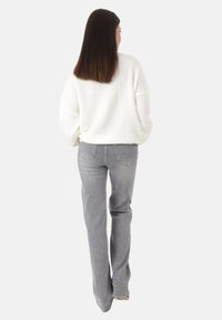 Jeans rectos de color gris claro con bolsillos traseros, combinados con un suéter de punto blanco de gran tamaño, vistos desde detrás. Textura suave, ajuste casual.
