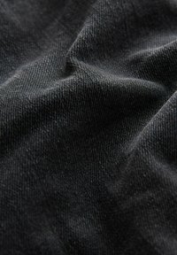 Tissu en denim noir avec une surface texturée, présentant une apparence légèrement froissée et des variations subtiles dans le tissage et la nuance.