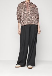 Wzorzysty hoodie z troczkiem, w odcieniach różu i czerni; zestawiony z luźnymi czarnymi spodniami i beżowymi butami.