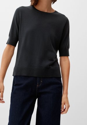 Czarny krótki sweter z krótkim rękawem, okrągłym dekoltem, teksturowaną tkaniną oraz prążkowanym dołem. W zestawieniu z ciemnoniebieskimi dżinsami.