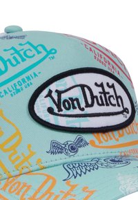 Casquette bleu-vert avec des logos et des motifs colorés, y compris du texte jaune et orange, avec un patch ovale noir proéminent affichant "Von Dutch."
