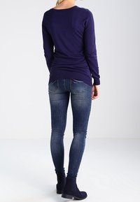 Musta pitkähihainen paita yhdistettynä istuviin sinisiin farkkuihin. Paidassa on pyöreä pääntie, ja farkuissa on haalistunut kuvio sekä takataskut.