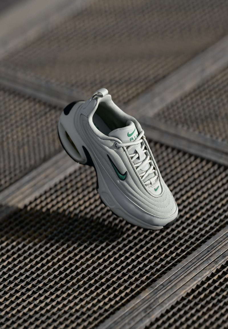 Heledad hall sneakers, millisegmente hinged upper, rohelised aktsendid ja paks valge tald. Omab ümarat varvaste piirkonda ja sidumisüsteemi.