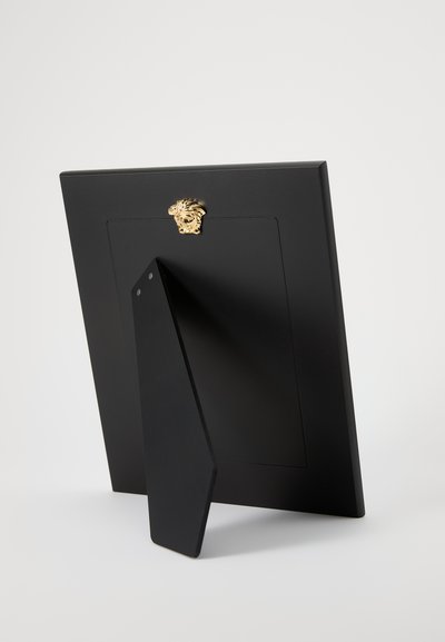 Melna foto rāmis ar zelta lauva galvas akcentu aizmugurē. Aprīkots ar stabilu statīvu un gludu matētu virsmu. Izgatavots, lai droši turētu fotogrāfijas.