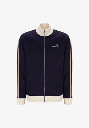 Giacca zip-up blu navy con colletto e polsini a coste color crema, con strisce laterali beige e un piccolo logo sul petto. Tessuto dalla superficie liscia.