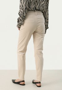 Beige elegantní kalhoty střihu slim, s švem na zadní straně, elegantním designem a v kombinaci s černými špičatými balerínami. Materiál je hladký a pevný.