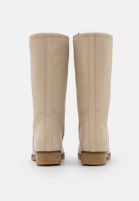 Botas de cuero beige hasta la rodilla con una textura suave, costuras en contraste y una suela de goma marrón resistente. Diseño sencillo sin adornos.