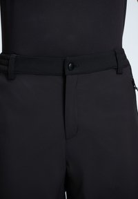 Zwarte broek van een soepel, rekbaar materiaal met een vlakke tailleband en een rits aan de voorkant. Inclusief een knoopsluiting en een zijzak met rits.