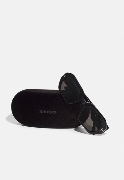 Ochelari de soare negri Tom Ford cu rame octogonale și lentile întunecate, așezați pe un etui moale negru cu numele brandului embosat.