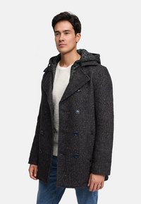 Abrigo marino de paño con diseño de doble botonadura, con capucha gris estampada, botones grandes y acabado texturizado. Combinado con una camisa clara.