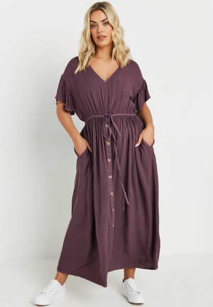 Vestido maxi de tela malva, con escote en V, mangas con volantes, cintura con cordón, botones en el frente y bolsillos laterales. Se lleva con zapatillas blancas.