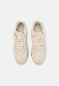 Béžové tenisky s vzorovanou texturou, šněrovacím designem a hladkou podrážkou. Interiér obsahuje měkké polstrování s logem "Calvin".