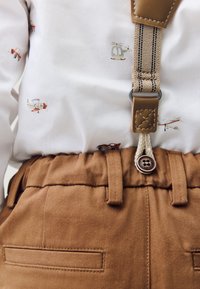 Brown cotton pants with a textured waistband, featuring a button and belt loops, paired with a white shirt that has small plane and helicopter patterns.