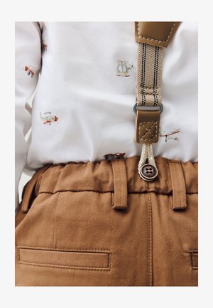 Pruunid puuvillased püksid tekstuurse vöökohtaga, millel on nupp ja vööaugud, kombineeritud valge särgiga, millel on väikesed lennuki ja helikopteri mustrid.