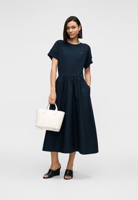 Μπλε μπλουζοφόρεμα με φούστα φαρδιά, κατασκευασμένο από βαμβάκι. Μαύρα σανδάλια slide και ένα μικρό λευκό χιαστί τσαντάκι ολοκληρώνουν το σύνολο.