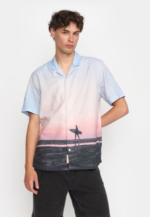 Chemise à manches courtes avec un bouton, présentant un dégradé du bleu clair au rose, avec un design de silhouette de surf sur une plage sombre.