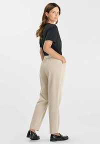 Beige, geribbelde, taps toelopende broek met zijzakken en een elastische tailleband, gecombineerd met een eenvoudig zwart t-shirt en zwarte schoenen.