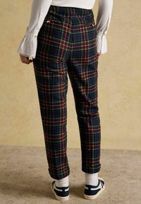 Svārki rūtainā rakstā tumši zils, zaļš un sarkans ar piegriezumu; ar sānu kabatām un jostasvietu ar pogu akcentiem; potīšu garuma.