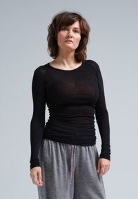 Schwarzes Langarmoberteil mit einer taillierten Passform, hergestellt aus einem transparenten Material. Kombiniert mit grauen, locker sitzenden Sweatpants mit Kordelzug.