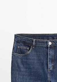 Mörkblå denimjeans med klassisk passform, med en framficka, metallknapp som stängning och sömmar längs midjebandet.