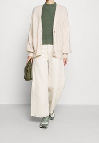 Beżowy kardigan z dzianiny z oversize'owymi rękawami, zielony sweter prążkowany, szerokie ecru spodnie i zielona torebka. Sneakersy z szarymi i białymi detalami.