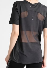 Camiseta atlética negra con espalda de malla, con cuello redondo, mangas cortas y un sutil logo de Nike. Puntos decorativos en la parte posterior.