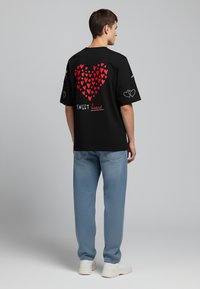 Black t-shirt with red heart pattern on back, "SWEET heart" text, and additional heart graphics on sleeves. Paired with light blue jeans.
