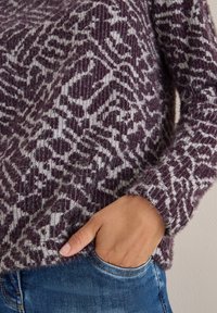 Sweter dzianinowy w bordowo-szarym schemacie kolorów z teksturowanym wzorem. Długie rękawy i luźny krój podkreślają miękki materiał.