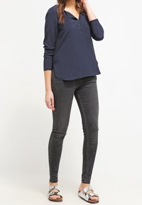 Blusa blu navy a maniche lunghe con colletto e dettagli di bottoni, abbinata a jeans skinny neri e sandali argentati con cinturini regolabili.