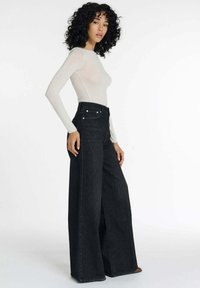 Zwarte wijde jeans gemaakt van denim, hoge taille met voorzakken en metalen details, gecombineerd met een aansluitend shirt met lange mouwen.