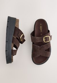 Paire de sandales en daim marron avec semelles noires et brides à boucles dorées, une sandale face vers le haut et l'autre sur le côté.