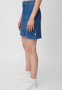 Jupe en denim bleu moyen avec une silhouette ajustée, dotée d'une fermeture à bouton sur le devant, d'un ourlet droit et d'un label de marque sur le côté.