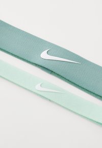 Dva preklopljena Nike platnena traka za glavu u svijetlozelenoj i mint zelenoj boji s bijelim Swoosh logotipom na bijeloj pozadini.