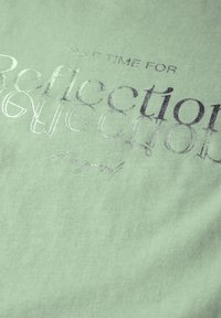 Un tissu vert clair présente un texte métallique argenté indiquant "PRENEZ LE TEMPS DE Réfléchir" avec un design de texte ondulé et une texture lisse.