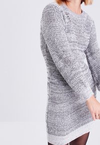 Robe pull en maille grise à manches longues, motif texturé et poignets côtelés. Matière douce, longueur genou avec un col rond.